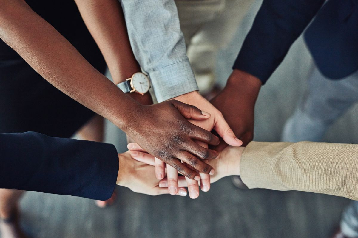 A group of diverse individuals placing their hands together in a stack, symbolizing teamwork and unity.